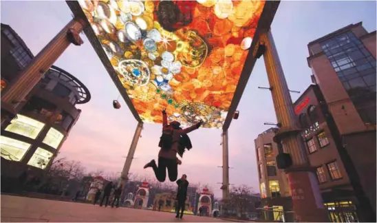  ??  ?? BEIJING: A woman jumps for a photo near an LED ceiling displaying images of gold and jewelry. — AP