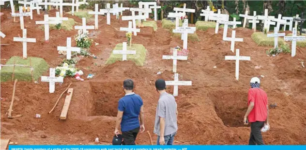  ??  ?? JAKARTA: Family members of a victim of the COVID-19 coronaviru­s walk past burial sites at a cemetery in Jakarta yesterday. — AFP