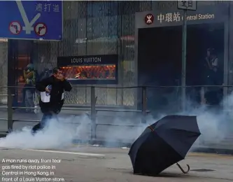  ??  ?? A man runs away from tear gas fired by riot police in Central in Hong Kong, in front of a Louis Vuitton store.