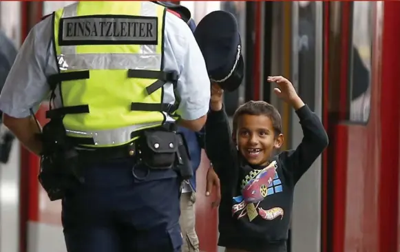  ?? MICHAEL DALDER/REUTERS ?? A security officer lets a boy try on his cap after a group of refugees arrived by train in Munich, Germany, this week.