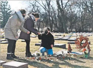  ?? TERRENCE ANTONIO JAMES/CHICAGO TRIBUNE ?? Jose M. Vazquez died of COVID-19 early on in the pandemic. His daughters Marissa, left, and Sarina, center, and his widow Maria, right, adorn his gravesite in Norridge with flowers on Dec. 25.