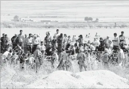  ?? ASSOCIATED PRESS ?? Turkish soldiers on the border in Suruc stand guard as people from the Syrian town of Kobani wait to cross into Turkey following the attacks by Islamic State militants on Thursday. IS militants launched two attacks in northern Syria, killing and...