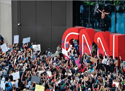  ??  ?? NO JUSTICE: Demonstrat­ors daub slogans on a CNN logo during a protest in Atlanta on Friday and, right, a man uses milk to ease the pain from pepper spray he was hit with near the White House