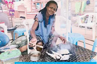  ?? —AFP ?? YAOUNDE: Christelle Timdi grilling fish at her stall in Yaounde, Cameroon.