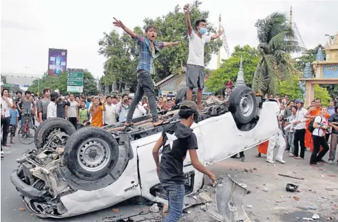  ?? EPA ?? Angry Cambodians stand on an overturned police car next to a polling station in Phnom Penh on Sunday after they couldn’t find their names on the voters list.