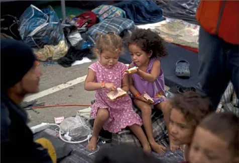  ?? Ramon Espinosa/Associated Press ?? Two girls, part of the migrant caravan, share a sandwich Wednesday at a shelter in Tijuana, Mexico. Migrants camped in Tijuana after traveling in a caravan to reach the U.S are weighing their options after a U.S. court blocked President Donald Trump’s asylum ban for illegal border crossers.