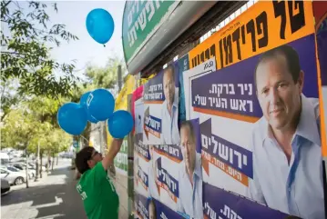  ?? (Baz Ratner/Reuters) ?? A SUPPORTER of the Meretz Party hangs balloons next to campaign posters of Jerusalem Mayor Nir Barkat, in the last election for city mayor in October 2013.