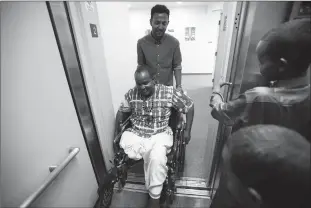  ?? Associated Press ?? Ali Said, of Somalia, center, is pushed by refugee caseworker Mohamed Yassin, behind, as he makes his way into an elevator with his two sons Thursday in San Diego. Said, whose leg was blown off by a grenade, says he feels unbelievab­ly lucky to be among...