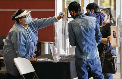  ?? Photos by Bob Owen / Staff photograph­er ?? Christina Farris checks the temperatur­es of the members of a young family as they check in for appointmen­ts at the CentroMed Noemi Eling Clinic on Walzem Road.