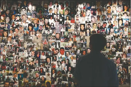  ?? (AP/Mark Lennihan) ?? Desiree Bouchat, a survivor of the 9/11 attacks on the World Trade Center, looks at photos of those who died in a display at the 9/11 Tribute Museum in New York. While Sept. 11 was a day of carnage, it also was a story of survival. Nearly 3,000 people were killed, but an estimated 33,000 or more people evacuated the World Trade Center and Pentagon.