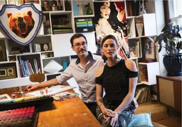  ?? MELISSA RENWICK PHOTOS/TORONTO STAR ?? Artists Yvan Semenowycz and Robyn Waffle seated at their dining/boardroom table with some of their work, including a Wonder Woman and grizzly bear designs, on display behind them.