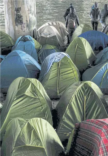  ??  ?? THIS IS HOME: Migrants stand by tents at a makeshift camp set under a bridge along the Canal de Saint-Deni