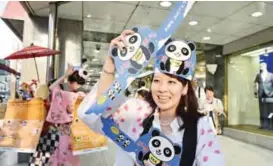  ??  ?? TOKYO: An employee of a department store in Tokyo’s Ueno shopping district distribute­s paper masks showing a baby panda to celebrate the birth of a baby panda at the nearby zoo.