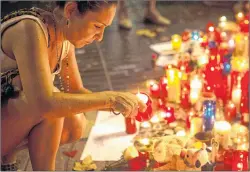  ?? (AP PHOTO/SANTI PALACIOS) ?? A woman lights up a candle at a memorial tribute to the victims of the vehicle attacks on Barcelona’s historic Las Ramblas promenade, in Barcelona, Spain, on Sunday.