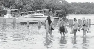  ?? JOE RAEDLE/GETTY ?? People walk to their boat through a flooded parking lot at the Haulover Marine Center in Miami Beach in August. King tides flooded the entire marina.