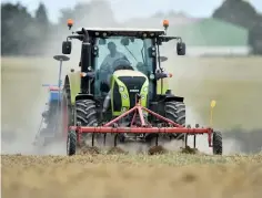  ??  ?? A farmer drives a tractor as he sows his field.