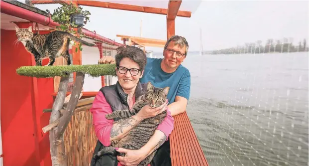  ??  ?? Ganz nah am Wasser: Laura und Stefan Bottke (mit Leo und Lilli) leben auf dem Fluss. Das feine Netz auf der Terrasse soll verhindern, dass die beiden Katzen baden gehen.