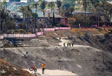  ?? ?? Firefighte­rs and residents stand Thursday on a fire road where the Coastal Fire jumped and burned several homes in Laguna Niguel.