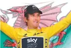  ?? Christophe Ena/AP ?? Geraint Thomas, wearing the overall leader’s yellow jersey, holds the Welsh flag on the podium on Sunday after the twenty-first stage of the Tour de France cycling race over with start in Houilles and finish on ChampsElys­ees avenue in Paris.