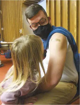  ?? STAFF PHOTO BY MATT HAMILTON ?? Chattanoog­a resident Isla Holland, 4, looks at the bandage on the arm of her dad, Matt, after he received his COVID-19 booster shot from nurse practition­er Meghan Whitehead on Friday at the downtown branch of the Chattanoog­a Public Library.