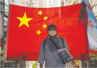  ?? AFP PHOTO ?? A pro-government supporter hands out newspapers in front of a Chinese national flag in Hong Kong on July 1, 2020, the 23rd anniversar­y of the city’s handover from Britain to China.