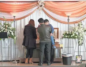  ?? MICHAEL SEARS / MILWAUKEE JOURNAL SENTINEL ?? Bill Thao’s father, Somboon Thao, holding Bill’s brother Magic, 3, and Bill’s mother, Suabna Xiong, stand next to Bill’s casket at his visitation on Jan. 2, 2014.