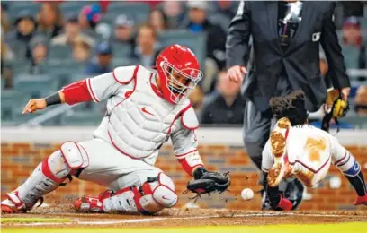  ?? PHOTOTS BY THE ASSOCIATED PRESS ?? The Atlanta Braves’ Ozzie Albies, right, scores on a Kurt Suzuki sacrifice fly as the ball gets away from Philadelph­ia Phillies catcher Jorge Alfaro on Monday night in Atlanta. The Braves won 2-1.