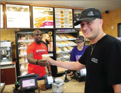  ?? Ernest A. Brown photo/The Call ?? New England Patriots’ safety Devin McCourty, left, is busy serving customers, including recent Bryant University graduate Chris Rae, of Providence, who stopped in to get an iced coffee at the Dunkin’ Donuts franchise on Smith Street in Providence...