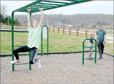  ??  ?? Kayla Hurley (left), 14, works her way across a set of monkey bars near Cooper Elementary School in Bella Vista while Mya Hurley, 9, talks with their father, John Hurley.
(NWA Democrat-Gazette/Keith Bryant)