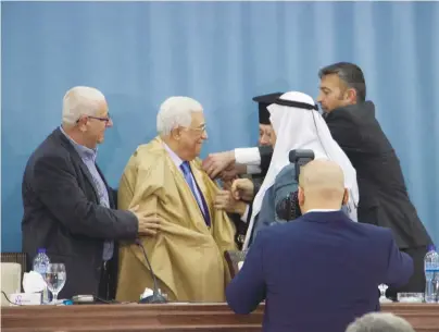  ?? (Adam Rasgon) ?? PA PRESIDENT Mahmoud Abbas tries on a robe given him by Christian and Muslim Israelis at an event in Ramallah on Thursday.