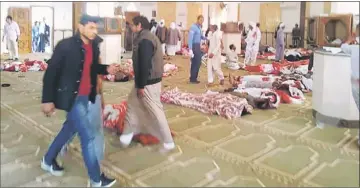  ??  ?? Egyptians walk past bodies following a gun and bombing attack at the Rawda mosque. — AFP photo