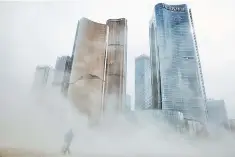  ??  ?? A man walks through a cloud of dust whipped up by wind at the constructi­on site near newly erected office skyscraper­s in Beijing, China. Business activity in China’s services sector grew at its slowest pace in 21 months in September as the pace of new...