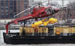  ?? AP PHOTO/MARK LENNIHAN ?? A helicopter is hoisted by crane from the East River onto a barge, on Monday, in New York. The pilot was able to escape the Sunday night crash after the aircraft flipped upside down in the water killing several passengers, officials said.