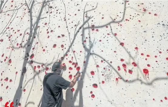  ?? AFP ?? An Iranian Kurdish Peshmerga member sprays red paint at holes in a wall made by shrapnel from a rocket attack days earlier at the party’s headquarte­rs in Koysinjaq, Iraq in September.