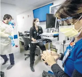  ?? JOSE A. IGLESIAS/MIAMI HERALD ?? Nurse Alix Zacharski, right, sanitizes her hands as other doctors and nurses continue to care for a patient in the Medical Intensive Care Unit for COVID-19 patients at Jackson Memorial Hospital on July 23.