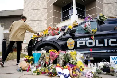  ?? The Associated Press ?? Q A man leaves a bouquet on a police cruiser parked outside the Boulder Police Department after an officer was one of the victims of a mass shooting at a King Soopers grocery store Tuesday in Boulder, Colo.