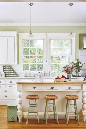  ?? ?? Color and a rich honey hardwood floor bring Leslie Saeta’s 100-year-old kitchen to life with a charming, repurposed island. Half-moon pulls add a cool contrast to the Shaker-style cabinets, while large windows over the sink bring in the light.