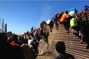  ?? — Reuters photo ?? Migrants climb the border fence between Mexico and the United States in an attempt to cross into the US side of the border in Tijuana, Mexico.