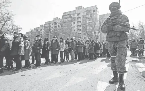  ?? REUTERS ?? Un soldado del ejército ruso vigila a residentes de Mariúpol que hacen cola para recibir ayuda humanitari­a