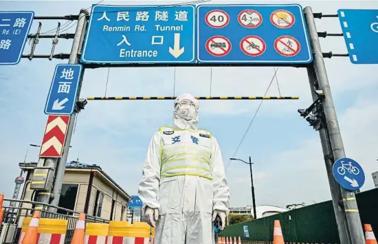  ?? HECTOR RETAMAL / AFP ?? Un agent de trànsit vestit amb un equip de protecció controla l’accés cap al barri de Pudong, en quarantena des d’ahir