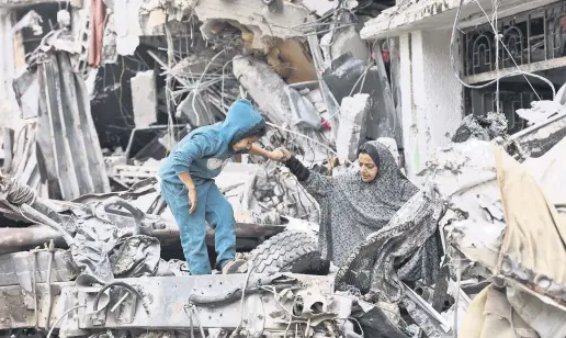  ?? ?? A Palestinia­n woman assists a child walking on the ruins of a building destroyed by Israeli bombardmen­ts, Gaza City, Palestine, April 8, 2024.