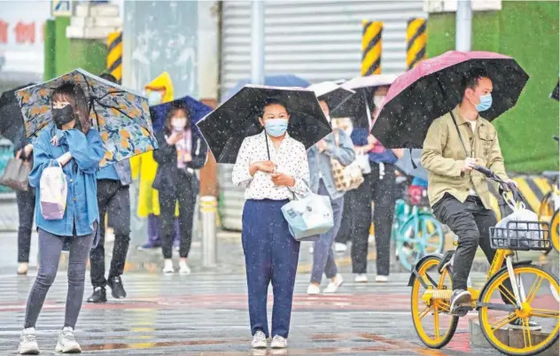  ?? Associated Press ?? ↑
Commuters wait to cross an intersecti­on on a rainy morning in Beijing.