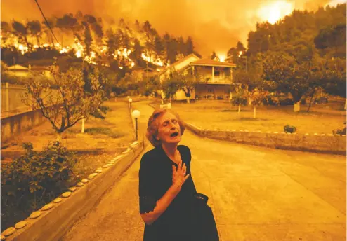  ?? KONSTANTIN­OS TSAKALIDIS / BLOOMBERG ?? An elderly resident reacts Sunday as a wildfire approaches her house in the village of Gouves, on the island of
Evia, where thousands of residents from dozens of villages were evacuated by boat.