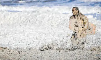  ?? FOTO: SEM VAN DER WAL/AFP ?? Ein Rettungshe­lfer trägt ein Board aus dem von schmutzige­m Schaum bedeckten Nordseewas­ser.