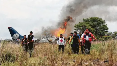  ?? Red Cross Durango via Associated Press ?? Rescue workers carry an injured person on a stretcher, as airline personnel walk away from the site where an Aeromexico airliner crashed Tuesday in a field near the airport in Durango, Mexico.