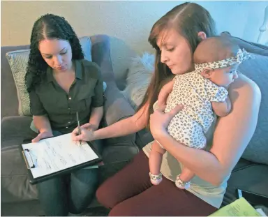  ?? PHOTOS BY DAVID WALLACE/THE REPUBLIC ?? Breanna Donaldson holds her daughter, Mazie, as she signs paperwork with Brianna Wiseman of Southwest Human Developmen­t at Donaldson’s Scottsdale home.