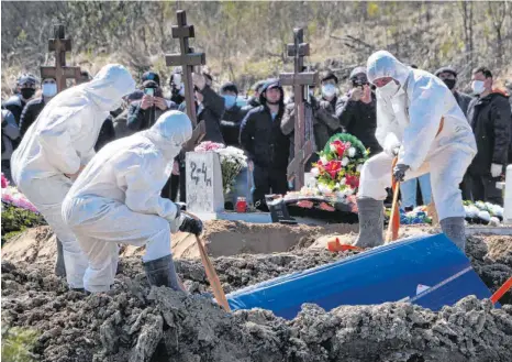  ?? FOTO: DMITRI LOVETSKY/DPA ?? Totengräbe­r in Schutzklei­dung lassen auf einem russischen Friedhof den Sarg eines Covid-19-Opfers in ein Grab, während Angehörige und Freunde in sicherer Entfernung stehen und zusehen. Verglichen mit anderen Ländern ist die Todesrate in Russland aber relativ gering.