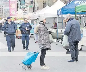  ?? Picture: AP ?? A shopper practises social distancing as police officers patrol the farmers market in Union Square on Wednesday in New York.