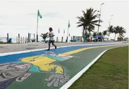  ?? — Reuters ?? Still interested: A woman running next to a graffiti depicting former star player Garrincha near Barra da Tijuca beach in Rio de Janeiro, Brazil, on Monday.