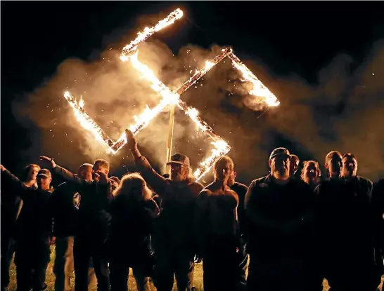  ?? GETTY IMAGES ?? Members of the National Socialist Movement, one of the largest neo-Nazi groups in the US, hold a swastika burning after a rally in Draketown, Georgia. The perpetrato­rs of some hate crimes are largely white men who hold the belief, exacerbate­d by rhetoric in politics and media, that they are protecting their culture, race and an endangered way of life.